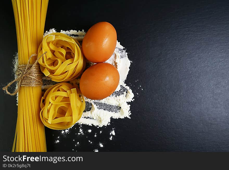 Different kinds of pasta tagliatelle, spaghetti, italian foods concept and menu design, raw eggs and flour on a shale board, empty