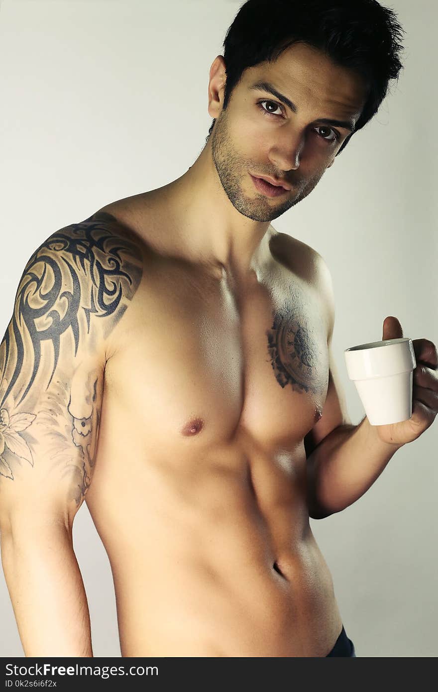 Tattooed Man With Bare Torso Is Holding A Cup