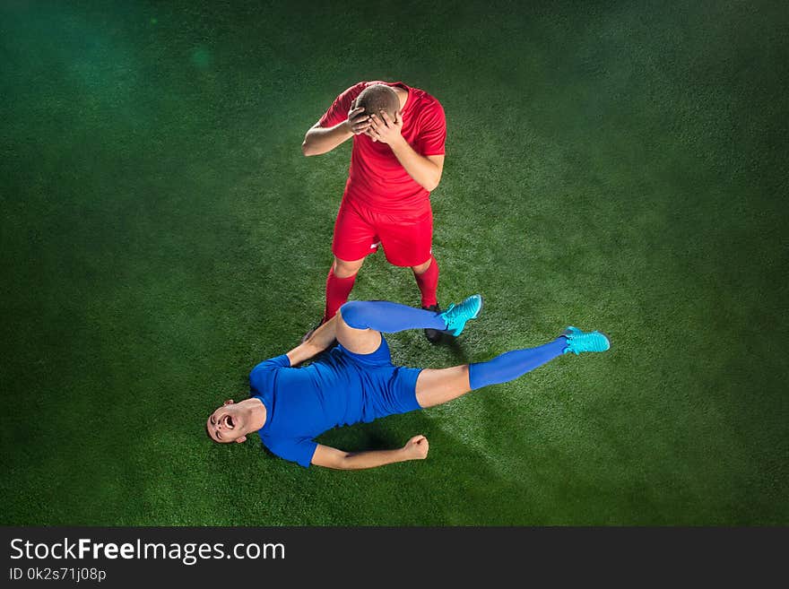 Male soccer player suffering from leg injury on football green field at stadium. The professional football, soccer player and human emotions concept. The players on green grass of football field background