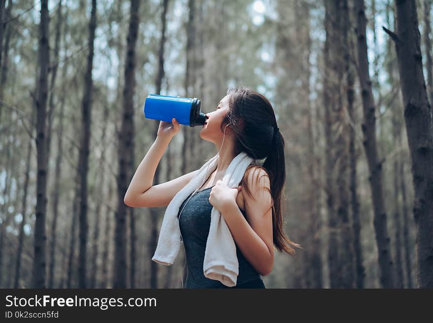 Beautiful asian woman drinking protein shake in the forest nature autumn for relaxing recovery healthy lifestyle with listening music with earphone sport outdoor.