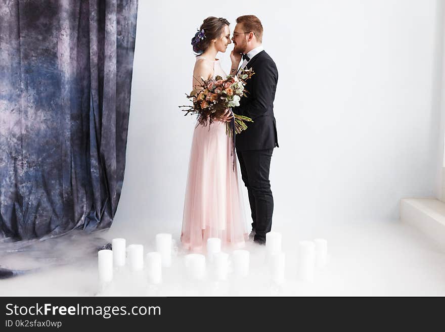 Full-length portrait of pretty newlyweds with bouquet. isolated white background. Studio horizontal shot with dry ice