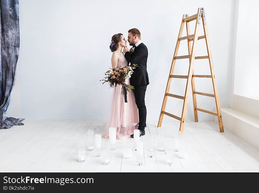 Happy bride and groom on ladder at studio. White wall background isolated