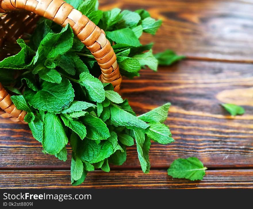 Bunch of mint in a small wicker basket on old burnt wooden background