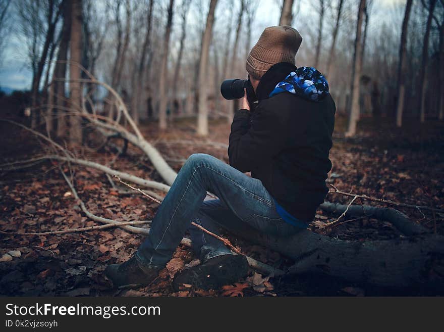 Man Wearing Black Jacket and Blue Jeans Sitting on Tree Branch