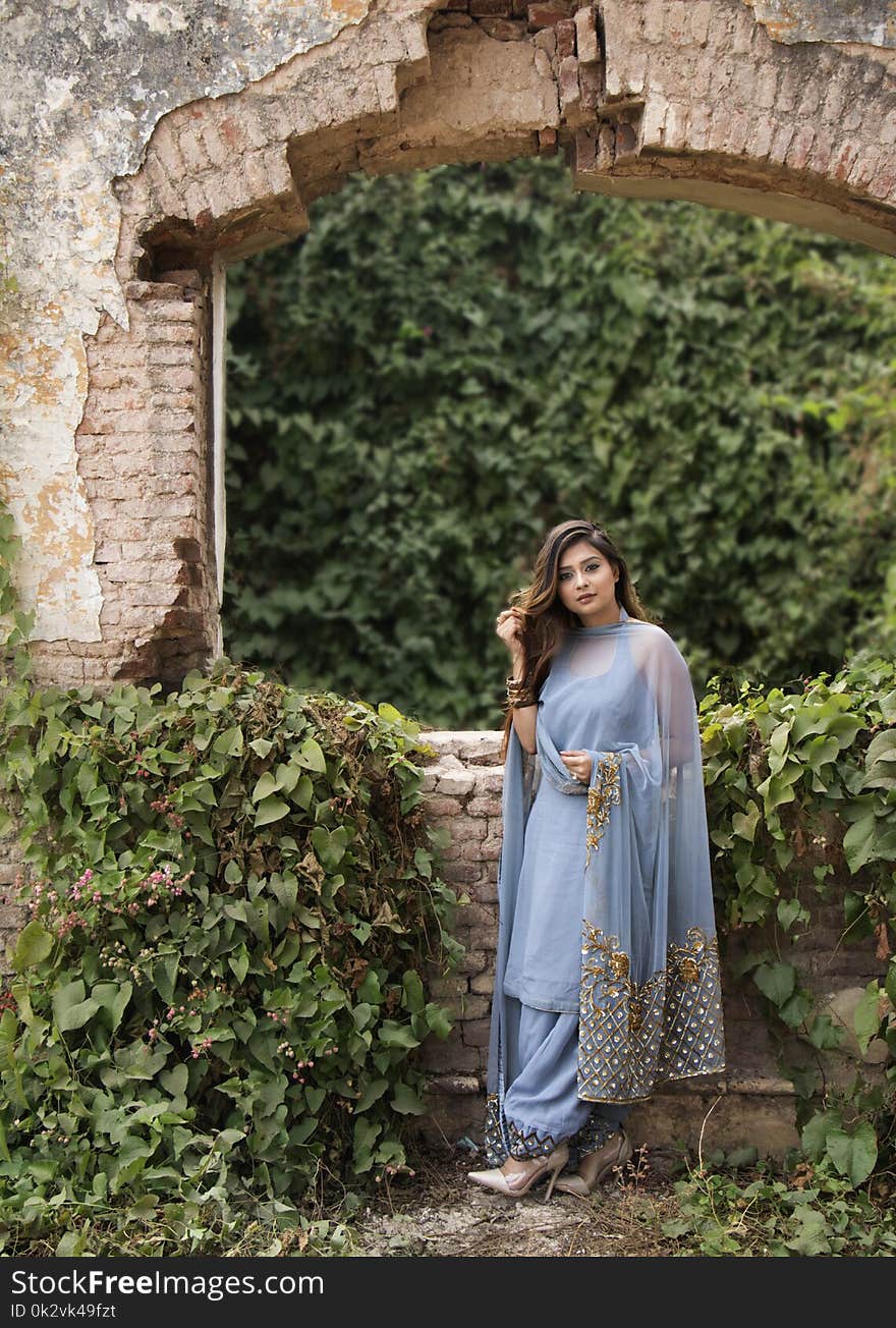 Woman in Blue Dress Standing Near Brown Concrete Bricks