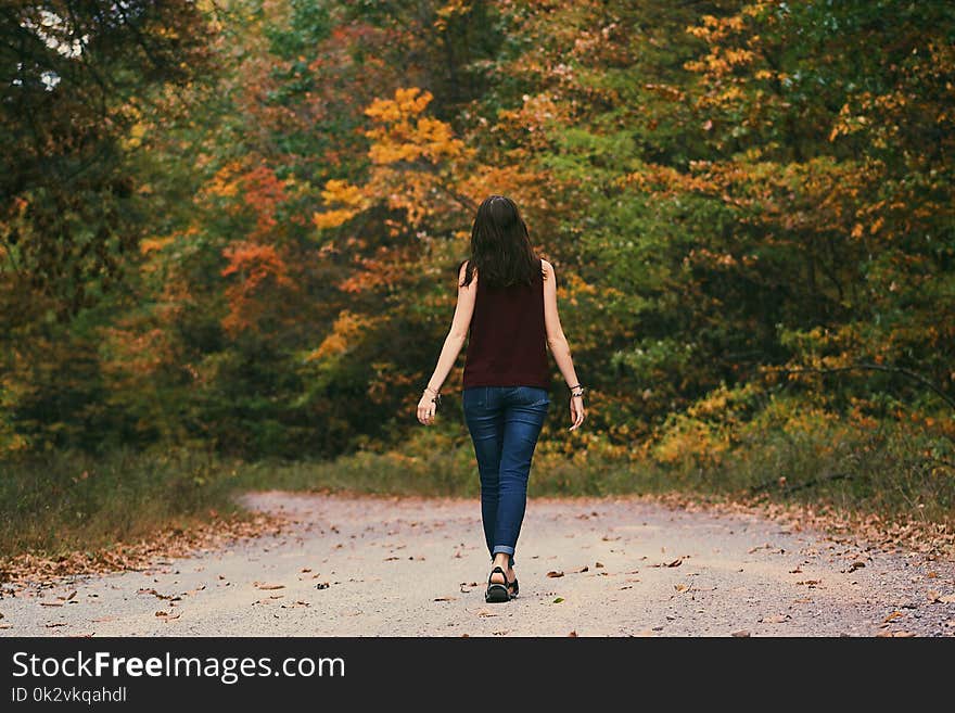 Woman in Brown Sleeveless Dress and Blue Jeans Standing on Gray Path Road