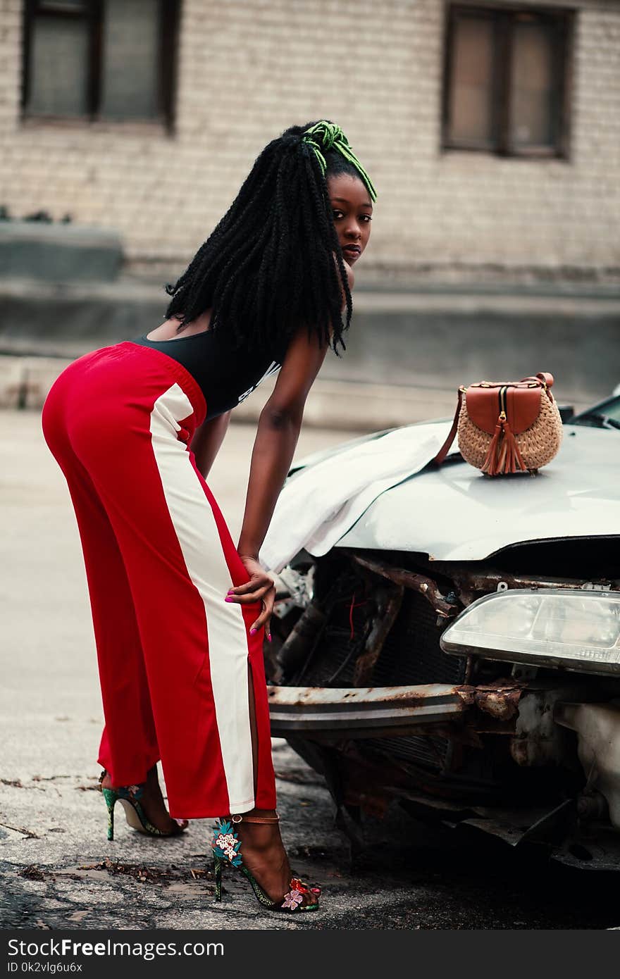 Woman in Maroon and White Pants Leaning in Front of Broken Car