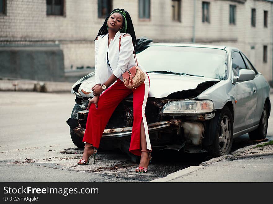 Woman in White Open Cardigan and Red and White Pants Sitting on Damage White Car