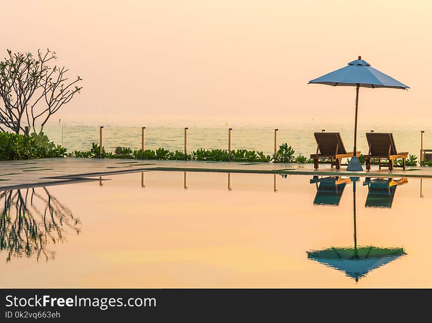 Beautiful umbrella and chair around swimming pool in hotel and resort in sunrise time