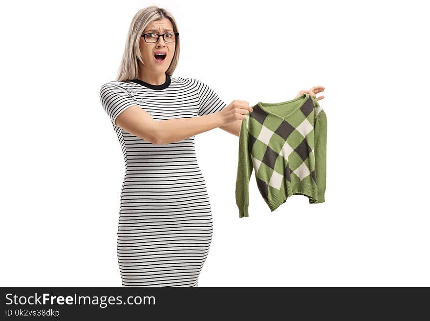 Shocked young woman holding a shrunken blouse and looking at the camera isolated on white background