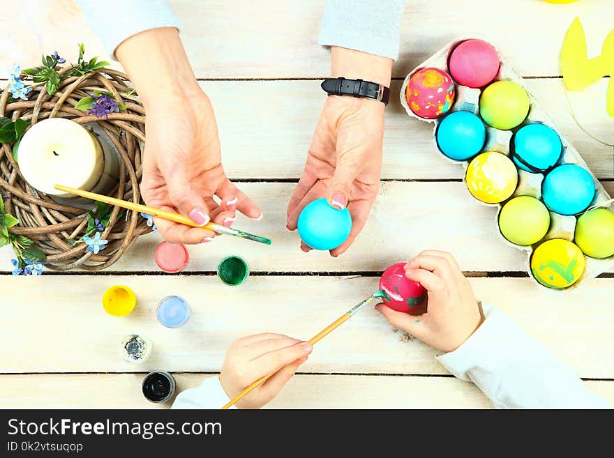 Mom and daughter draw on Easter eggs on a wooden background.