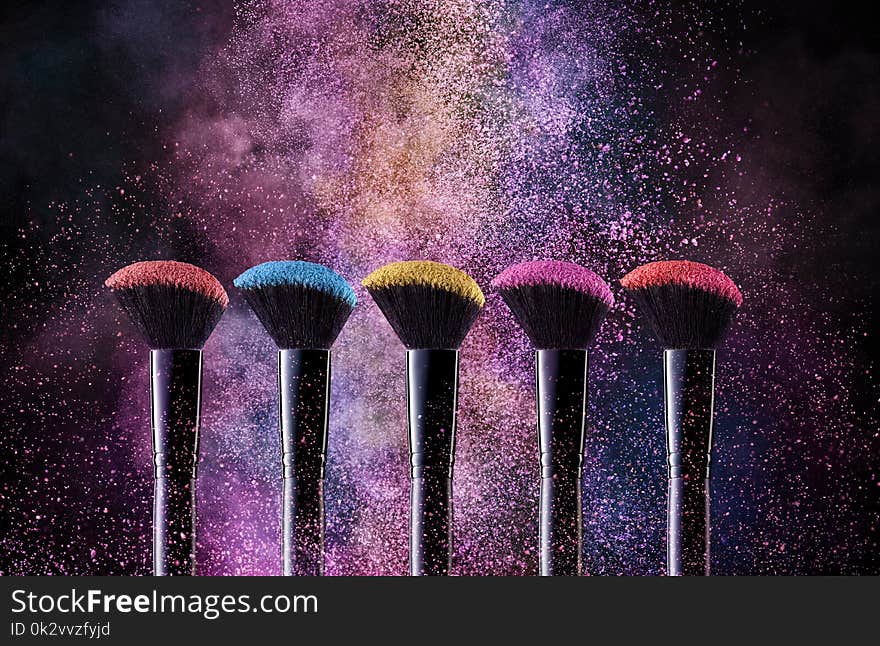 Cosmetic Brushes And Explosion Colorful Powders. Close Up Of Makeup Soft Blush Brushes Releasing Cloud Of Bright Powder Splash On Black Background. Makeup Tools. High Quality Image.