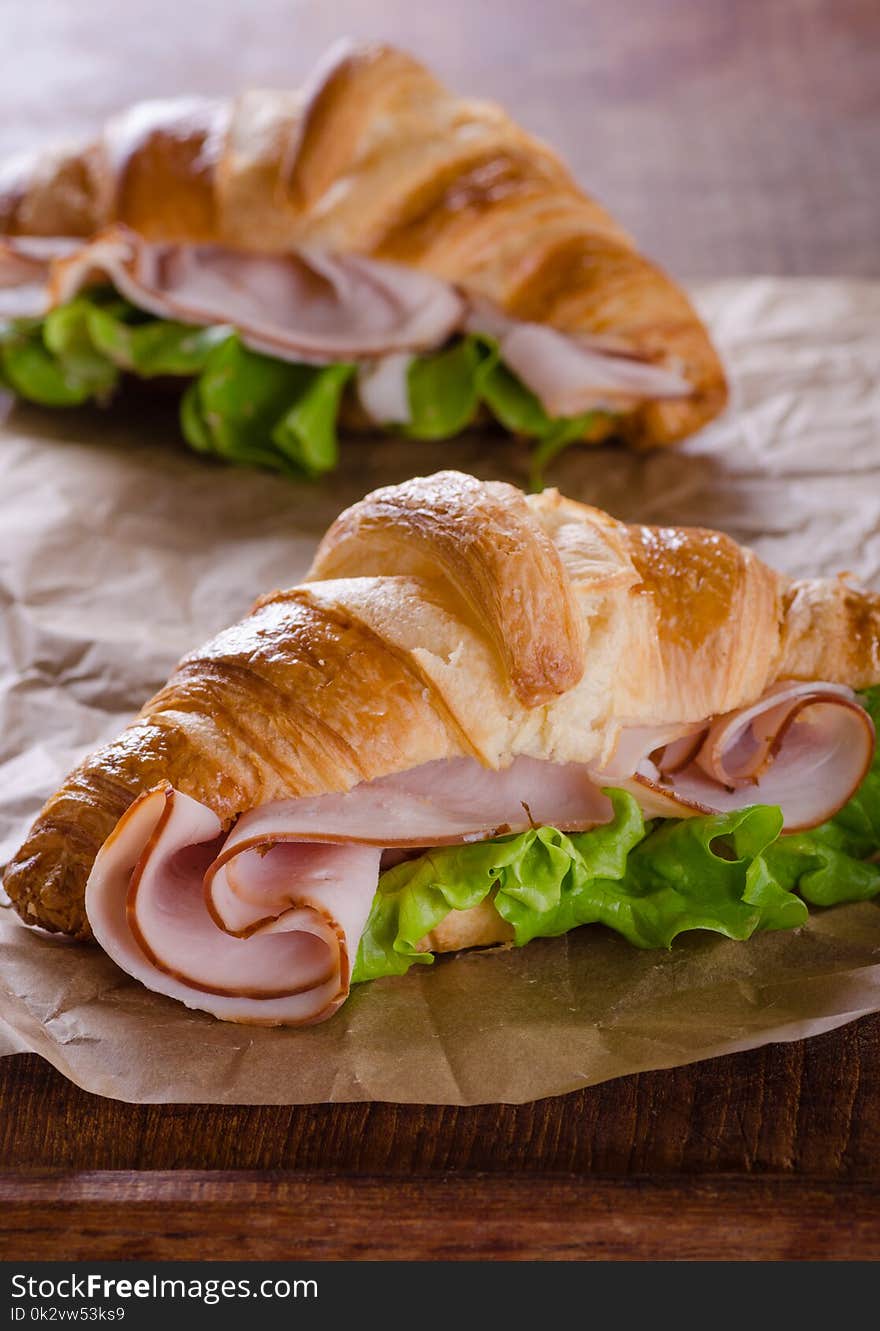 Fresh croissant sandwich with ham and salad leaf on baking paper. Fresh croissant sandwich with ham and salad leaf on baking paper