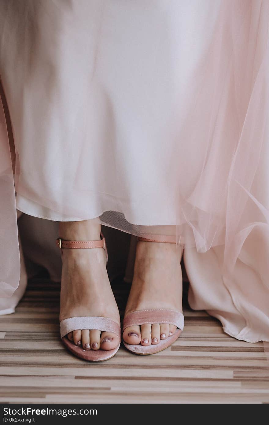 Bride`s legs close-up in velvet pink shoes and pink wedding dress transparent fabric. Vertical