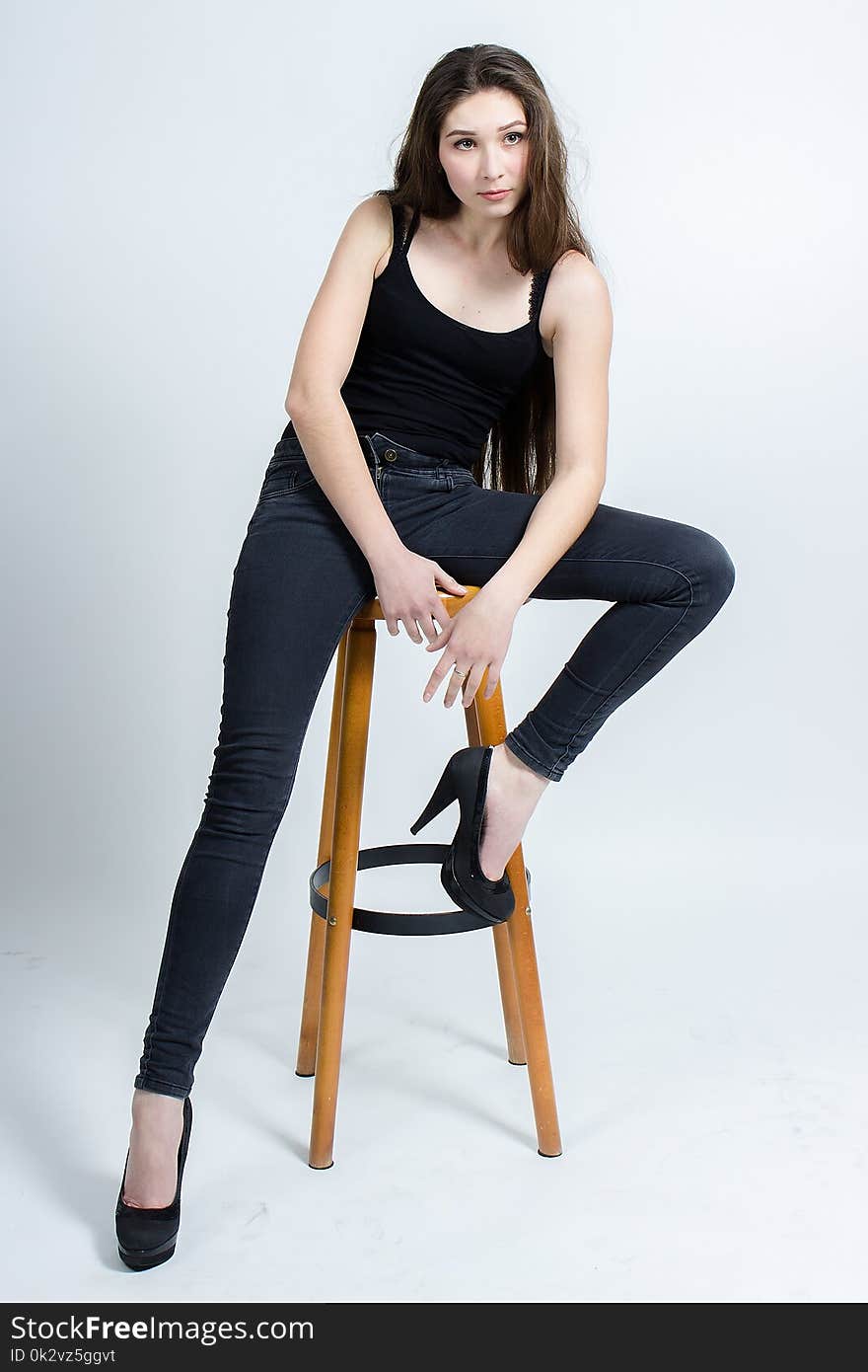 Girl with long dark hair posing on chair, black tank top jeans