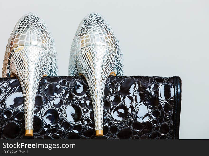 Elegant outfit, fashion concept. Black leather shiny handbag and silver high heeled shoes, closeup on gray. Studio shot. Elegant outfit, fashion concept. Black leather shiny handbag and silver high heeled shoes, closeup on gray. Studio shot.