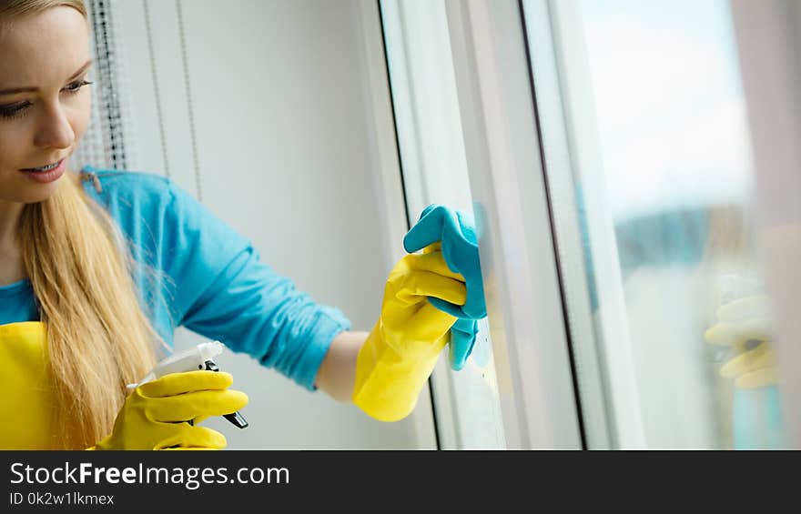 Young woman in yellow gloves cleaning window with blue rag and spray detergent. Spring cleanup, housework concept. Young woman in yellow gloves cleaning window with blue rag and spray detergent. Spring cleanup, housework concept