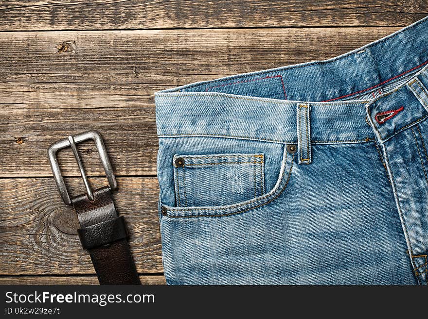 Blue Jeans and leather belt on wooden background, top view