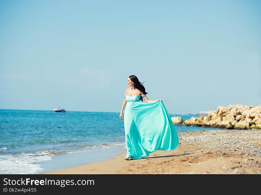 Young Woman In A Blue Dress Is Walking Along The Beach