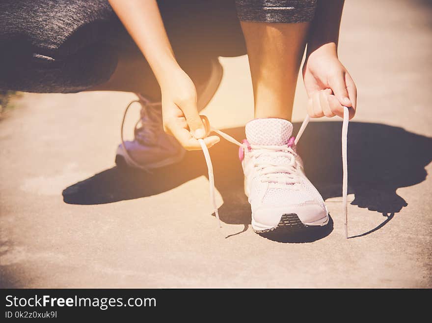 Hands of a young woman shoelace and sneakers. Shoes standing on the pavement of stones in the morning for for exercise