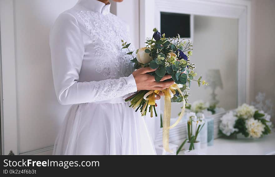 Beautiful bouquet of flowers in hands of young bride dressed in white wedding dress, close up