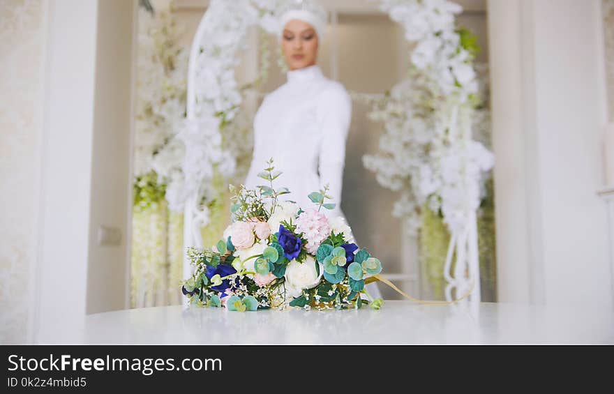 Beautiful bride in white traditional muslim dress with bunch of flowers, posing in studio