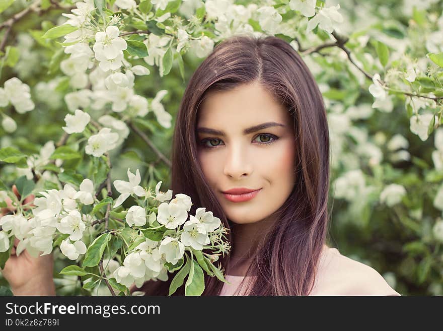 Beautiful female face closeup portrait. Pretty woman in blossom spring flowers background