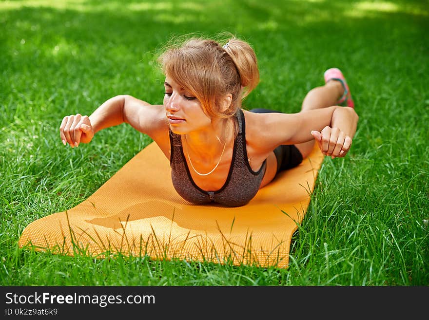 Young girl doing exercises on the mat in the park on the green grass