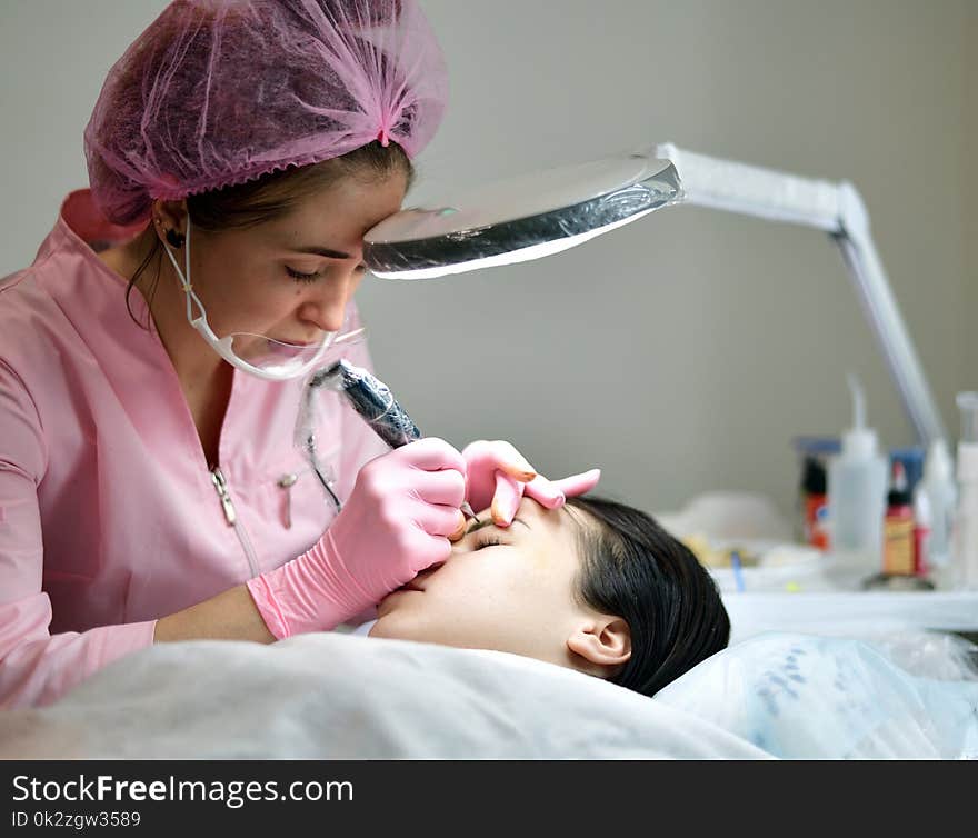 the master does the tattoo on the eyebrows to the girl. the master does the tattoo on the eyebrows to the girl.