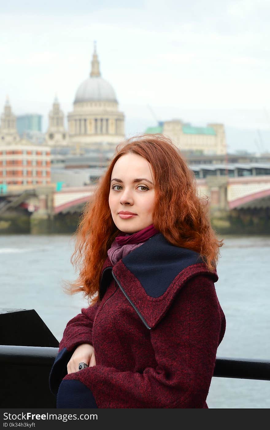 London girl. Portrait of beautiful smiling happy young woman near the Thames river on the background St Paul`s cathedral in London. Caucasian girl with red hair with St. Paul`s Cathedral on the background.