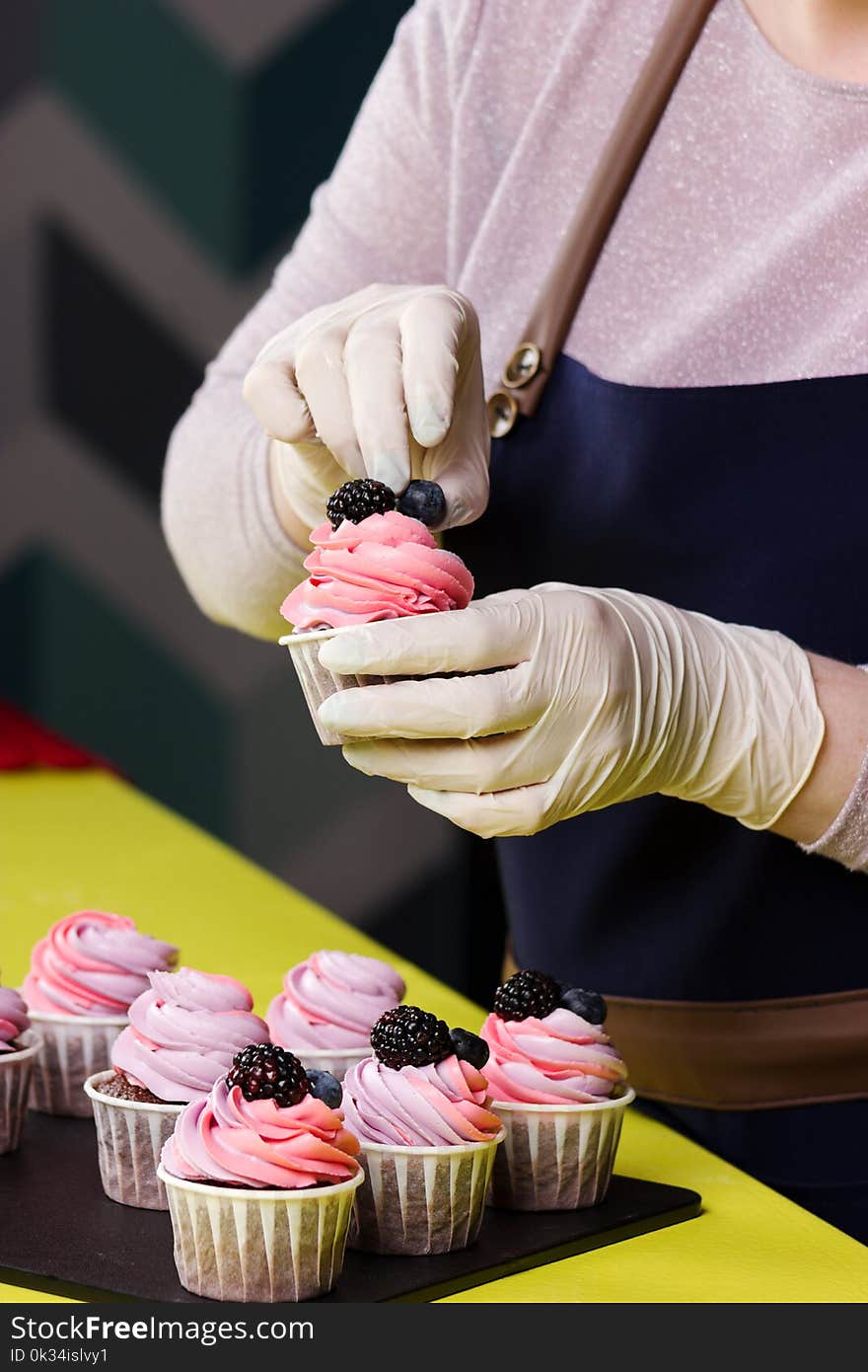 Woman decorating cupcakes with berry on the table in kitchen