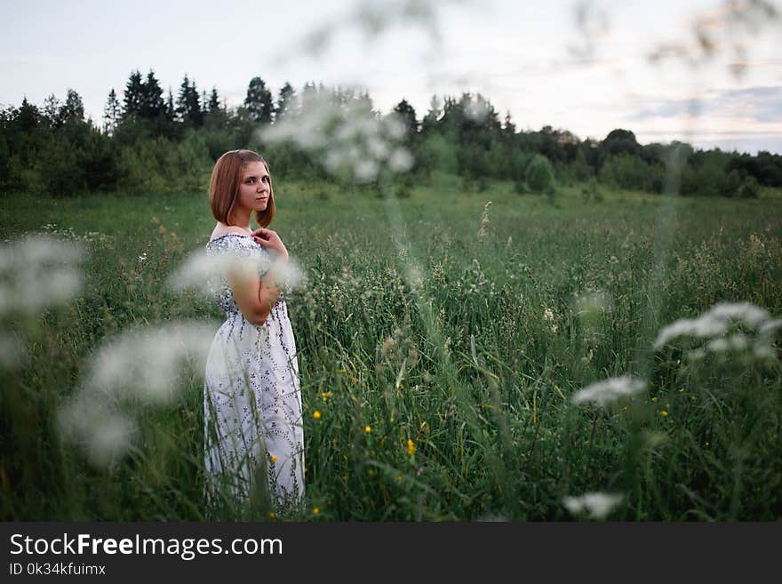 Beautiful brunette in the evening summer field with bouquet of meadow flowers.