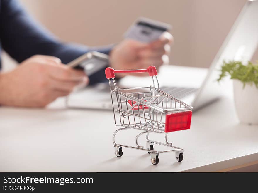 Bank Card Nearby A Laptop And Mini Shopping Cart On White Background Top View.