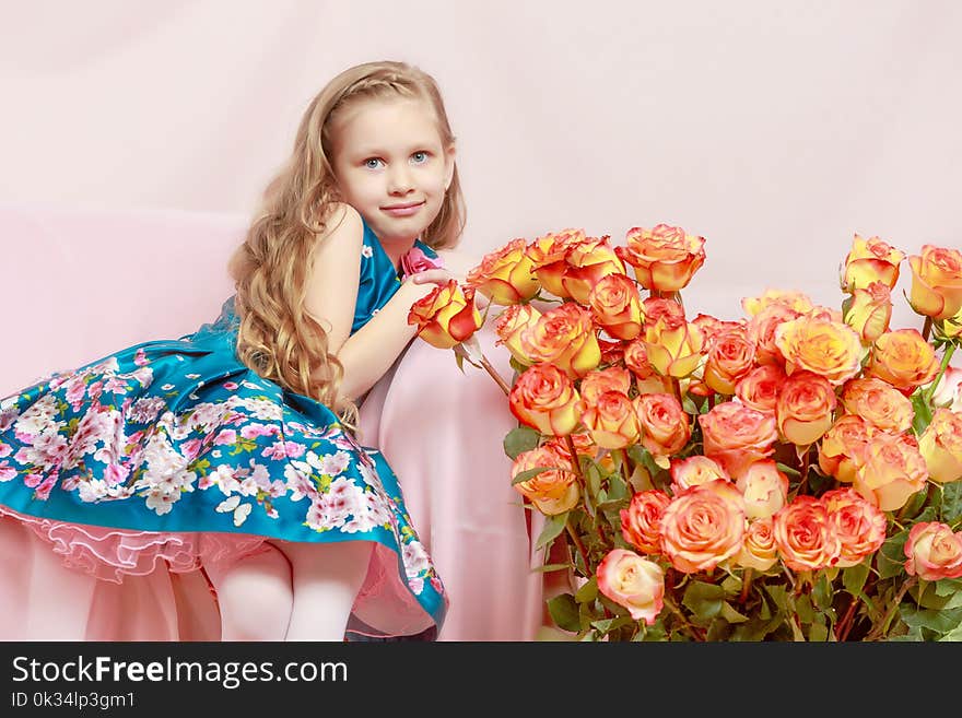 A beautiful little girl with long, light, curly hair, in a blue long skirt. She sits on a pink couch beside a large bouquet of tea roses. A beautiful little girl with long, light, curly hair, in a blue long skirt. She sits on a pink couch beside a large bouquet of tea roses.