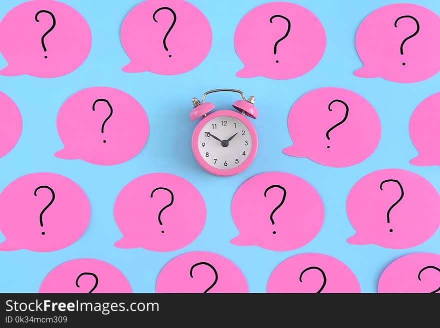 Pink stickers with question marks. A small pink alarm clock in the center. Bright photo from the top. Unusual background.