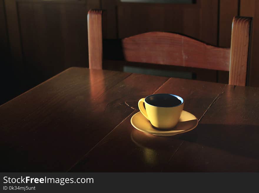 A yellow cup of coffee, with a soft ray of moonlight coming from the window