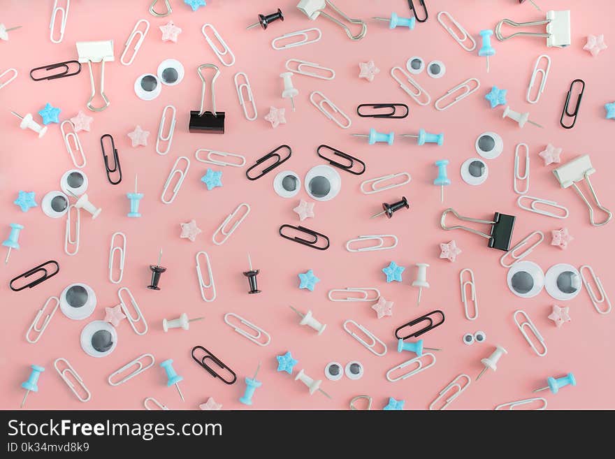 Beautiful pink background with white and black stationery. Staples, office buttons and asterisks are in disarray. In the center is a surprised smiley from clips and puppet eyes. Beautiful pink background with white and black stationery. Staples, office buttons and asterisks are in disarray. In the center is a surprised smiley from clips and puppet eyes.