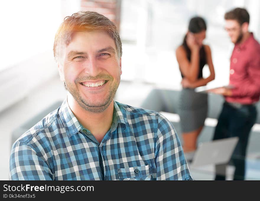 Handsome businessman is looking at camera and smiling while standing with crossed arms in office, his colleagues are working in the background. Handsome businessman is looking at camera and smiling while standing with crossed arms in office, his colleagues are working in the background