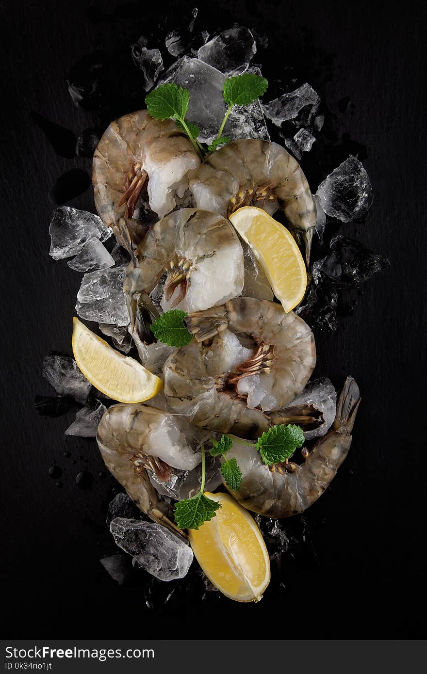 Fresh raw king prawns with lemon and lemon balm on dark slate kitchen plate with napkin can be used as background