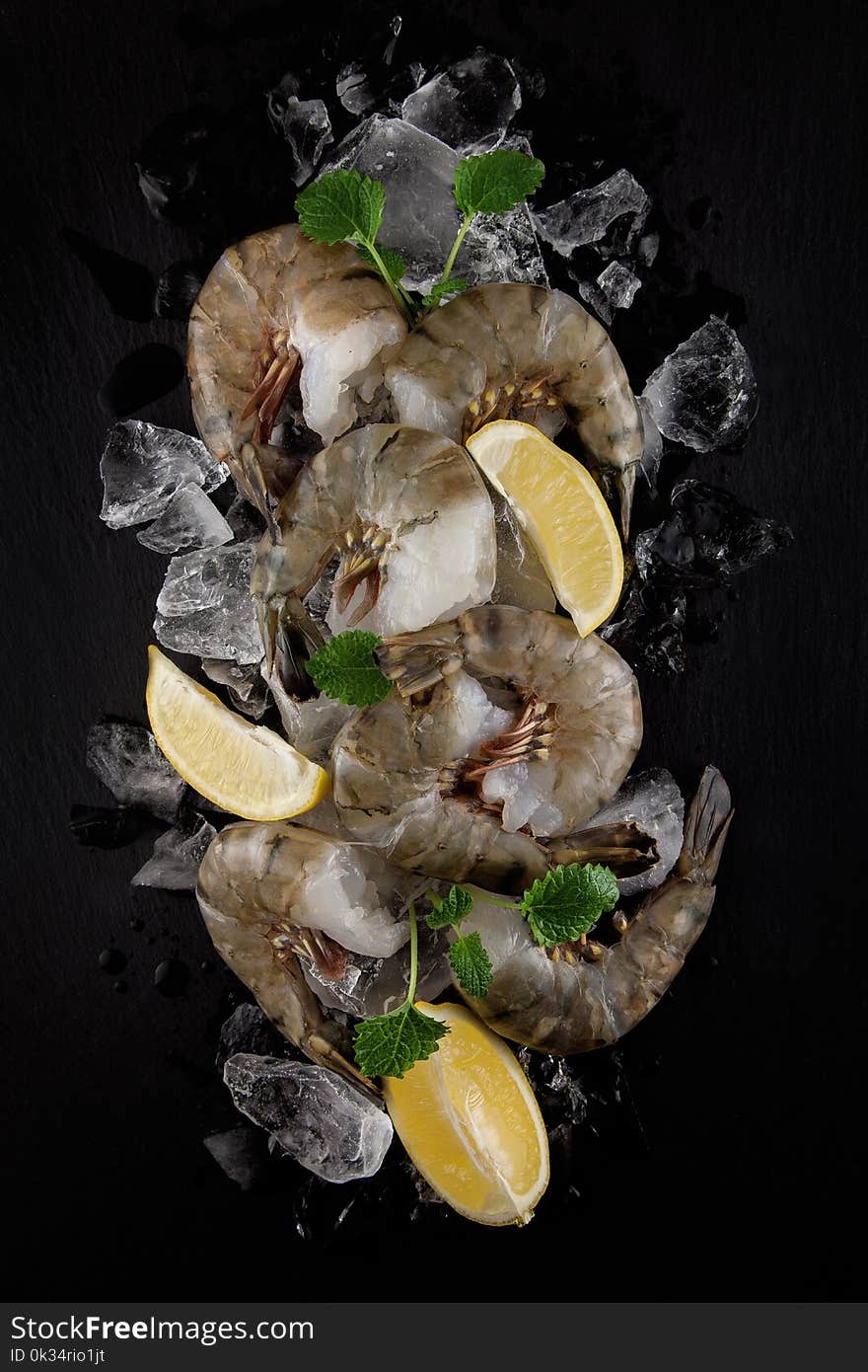 Fresh raw king prawns with lemon and lemon balm on dark slate kitchen plate