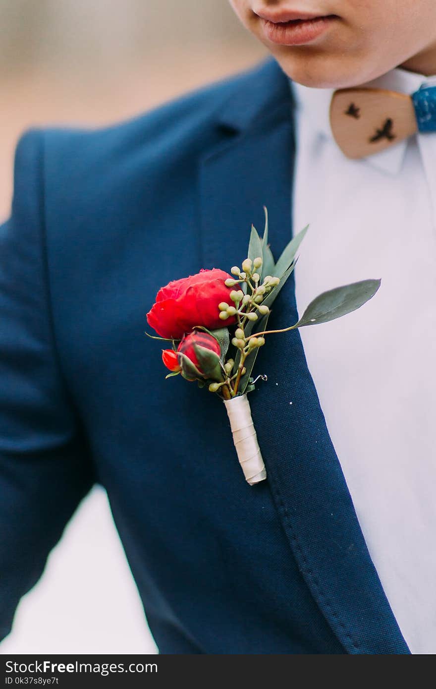 Red boutonniere in the grooms jacket close up.