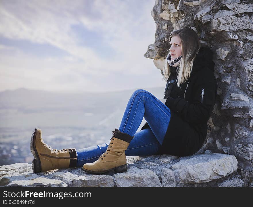 Woman in Black Coat Sitting on Rock