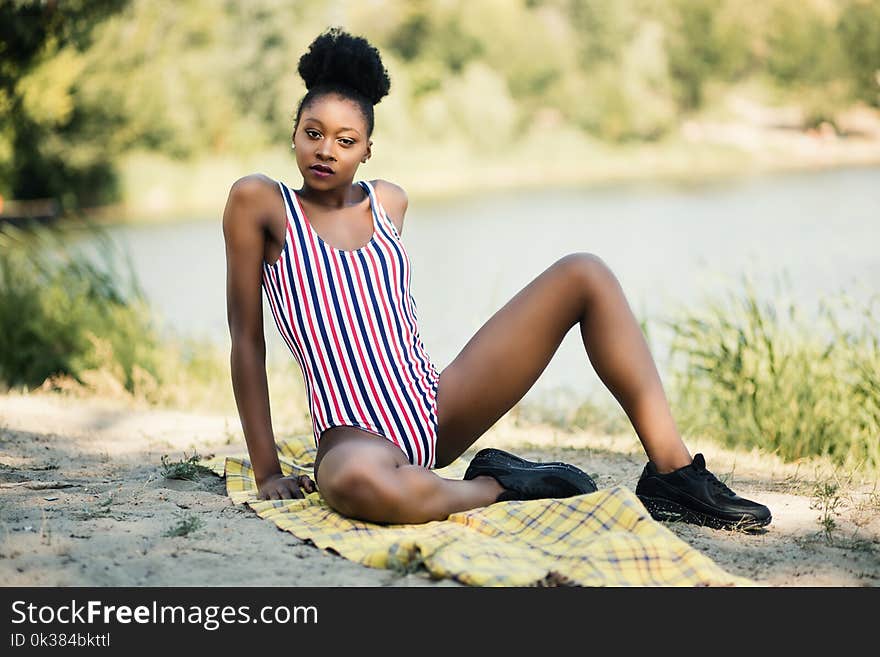 Woman in White, Red, and Blue Striped One-piece Suit Sitting Near River