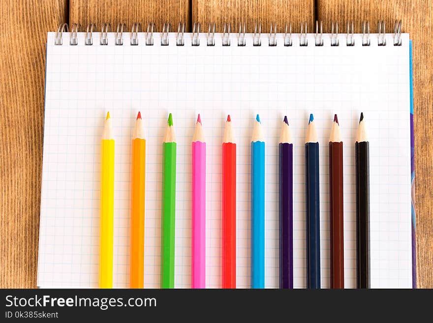 Set of colored pencils on school notebook on wooden background .