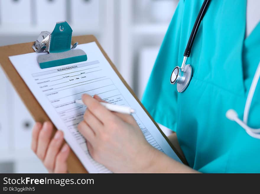 Female doctor filling up medical form on clipboard closeup. Physician finish up examining his patient in hospital and ready to give a prescription to help. Healthcare, insurance and medicine concept.