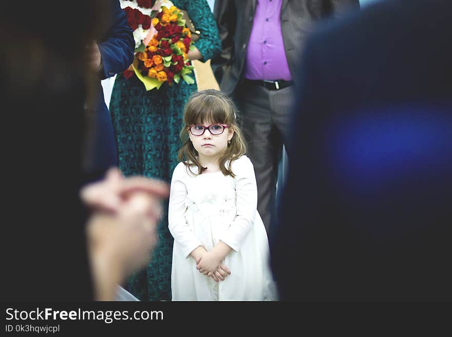 Sad little girl in white dress in the crowd at the wedding.