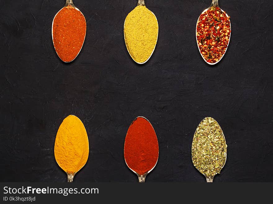 Spices in silver spoons, turmeric, paprika, cardamom, basil. On a wooden table. View from above.