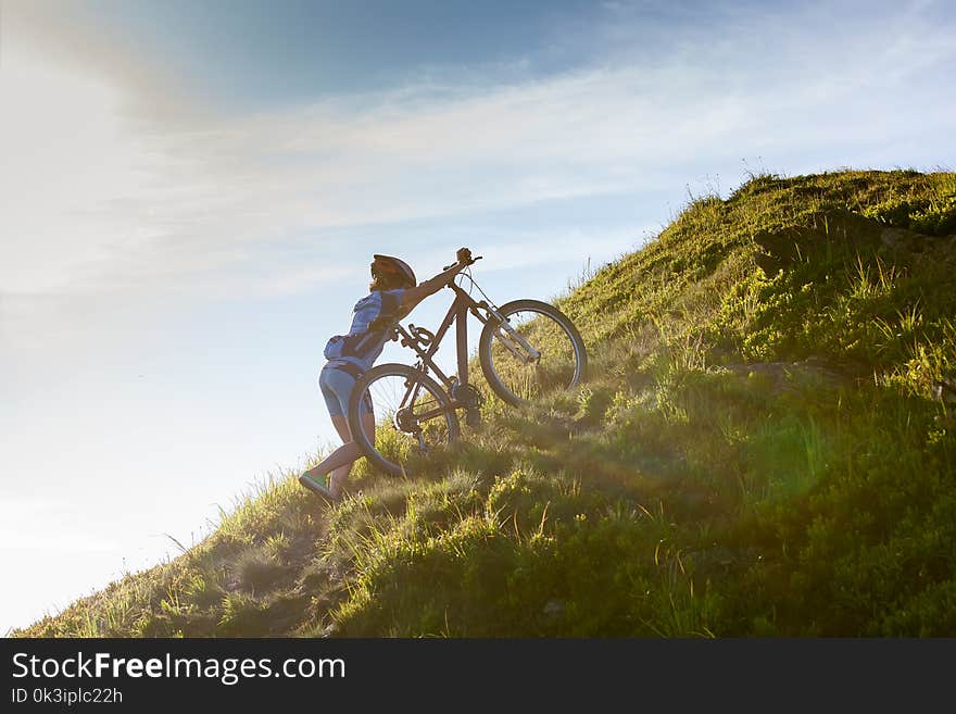 Biker pushes bicycle up in the mountains.