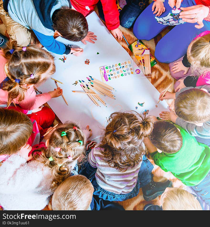 Several small children draw on a sheet of paper with pencils. A view from above.Child drawing top view. Artwork workplace with creative accessories. Flat lay art tools for painting.