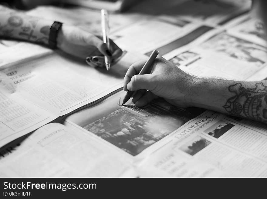 Grayscale Photo of Hands Writing on the Newspaper